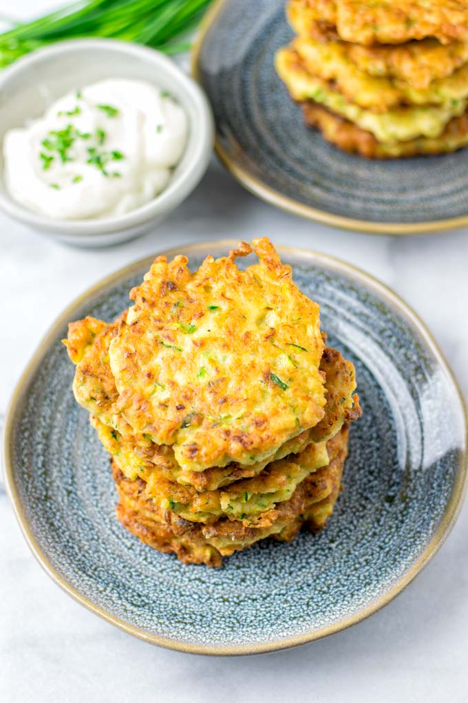 Stack of Zucchini Fritters on a blue plate with a small bowl of dip in the background.