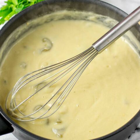 Ready White Enchilada Sauce with a wire whisk in the pot.