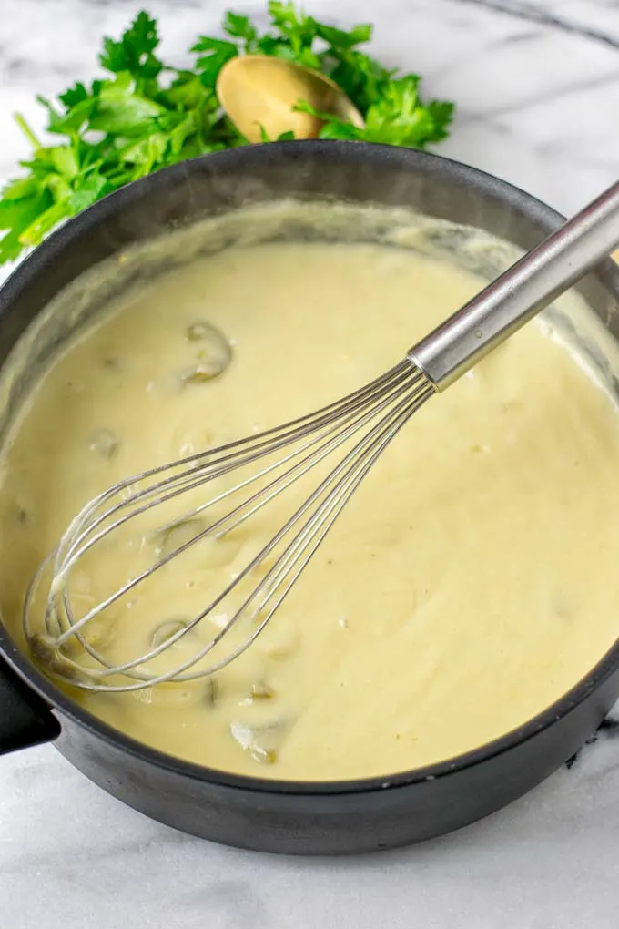 Ready White Enchilada Sauce with a wire whisk in the pot.