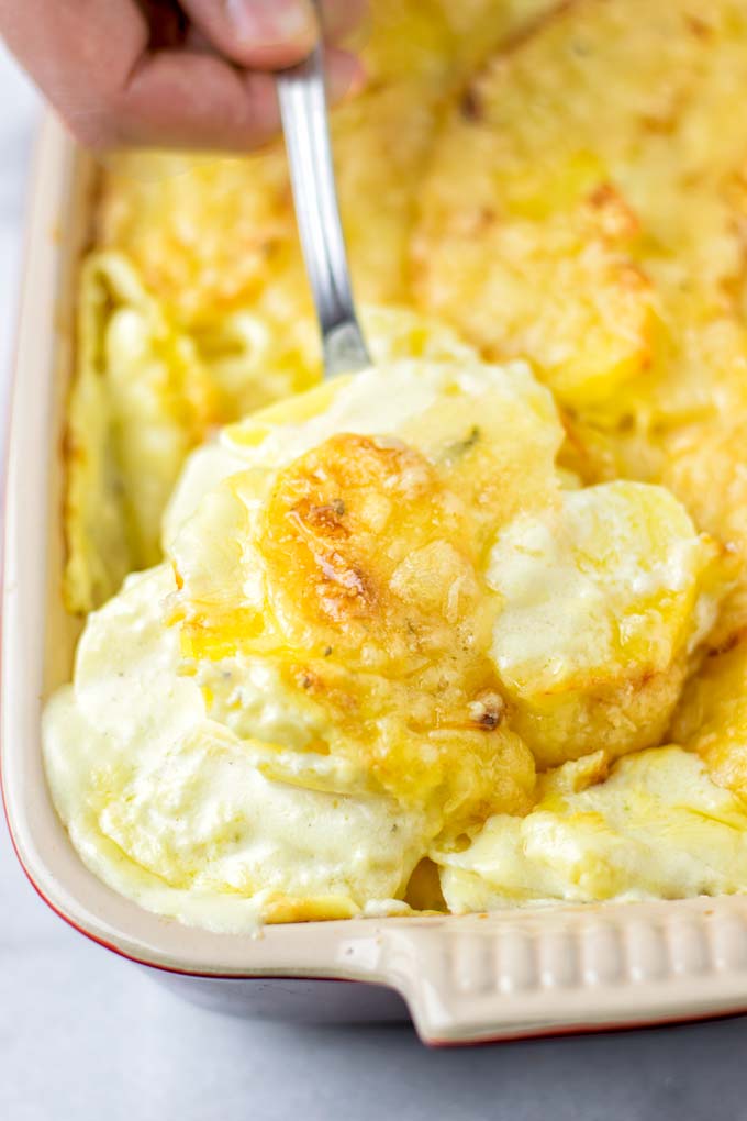 Lifting a spoonful of the Dauphinoise Potatoes out of the cooking pan.