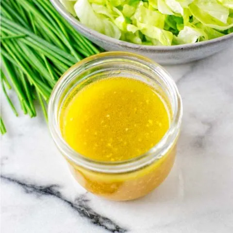 A glass jar of the Lemon Vinaigrette in front of a green salad.