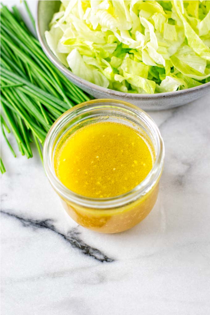 A glass jar of the Lemon Vinaigrette in front of a green salad.