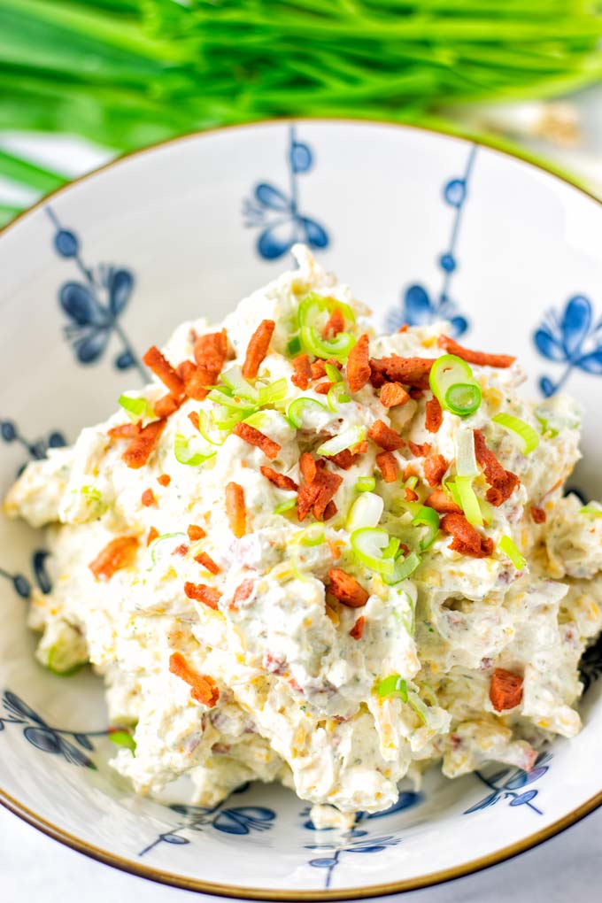 Closeup view of the vegan Crack Dip in a white jar. Dip is garnished with extra bacon bits and scallions.