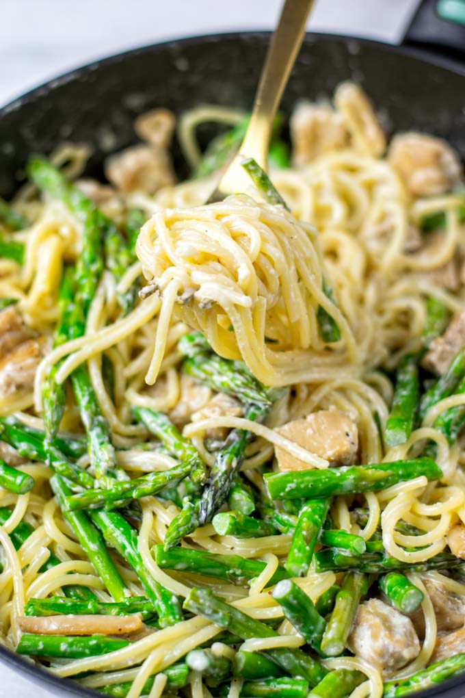 Closeup view of spaghetti curled on a fork, showing asparagus tips and vegan chicken.