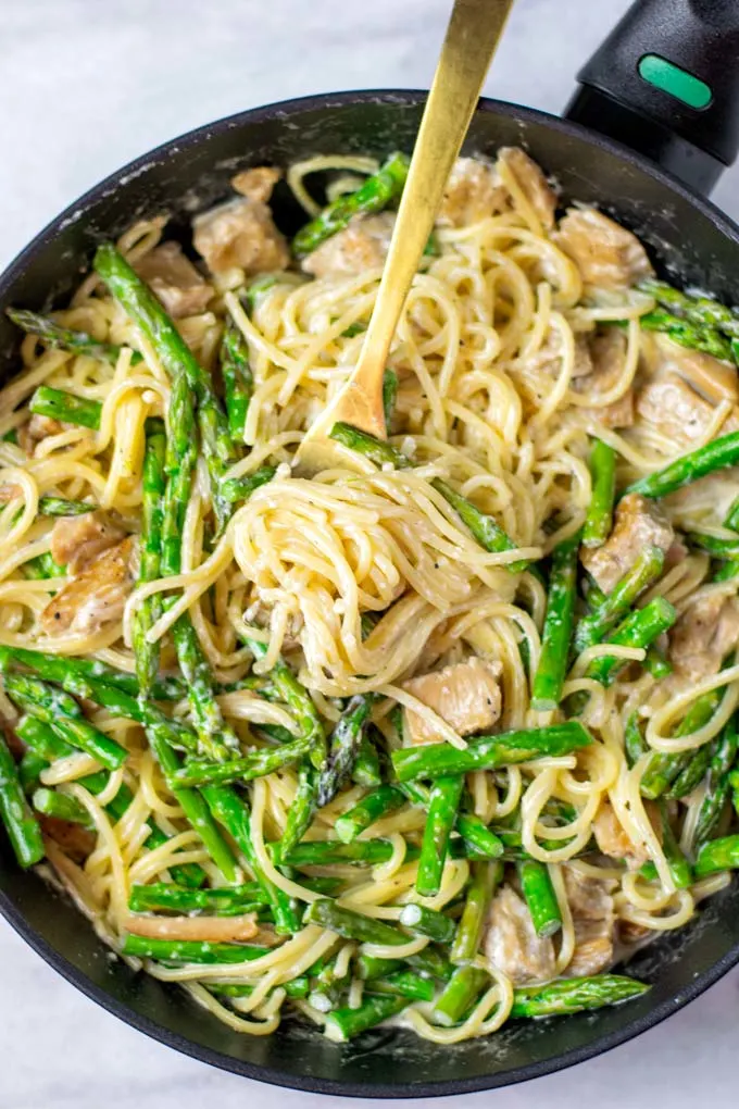 Top view on a sauce pan full of the finished Asparagus Pasta dish, with a golden fork.