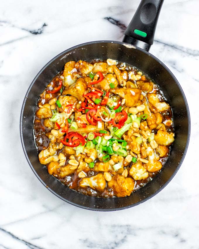 Top view on the Kung Pao Cauliflower in a sauce pan, garnished with fresh chili and scallions.