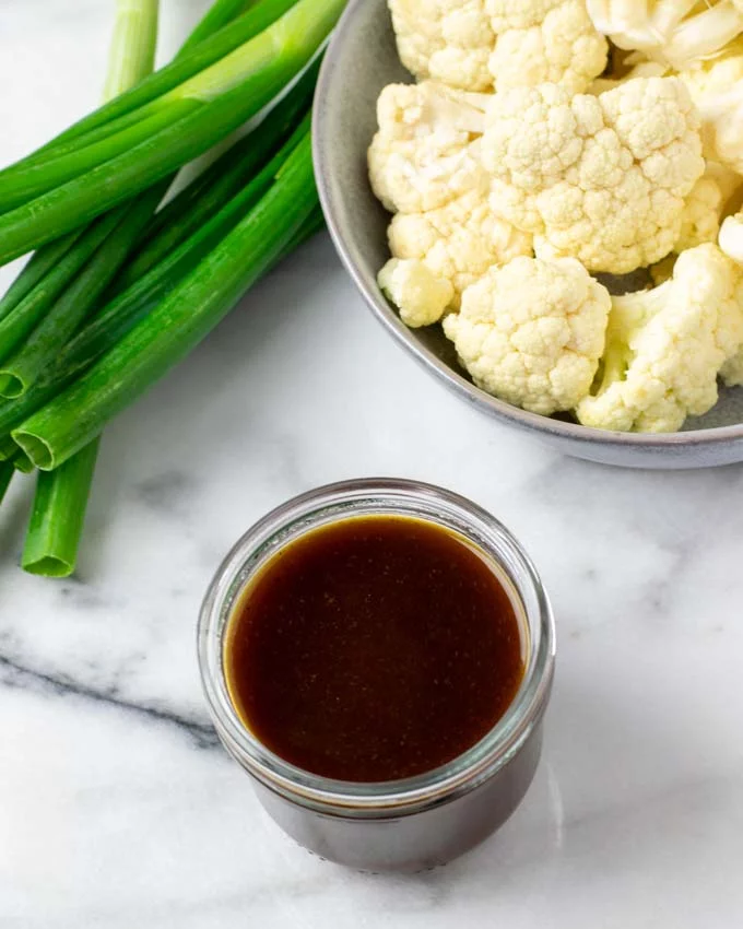 Kung Pao Sauce in a small glass jar with cauliflower and scallions in the background.