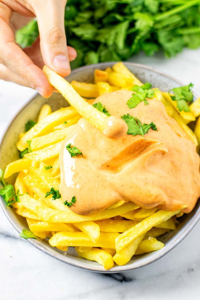 A hand is dipping a single fry into the Cajun Sauce.