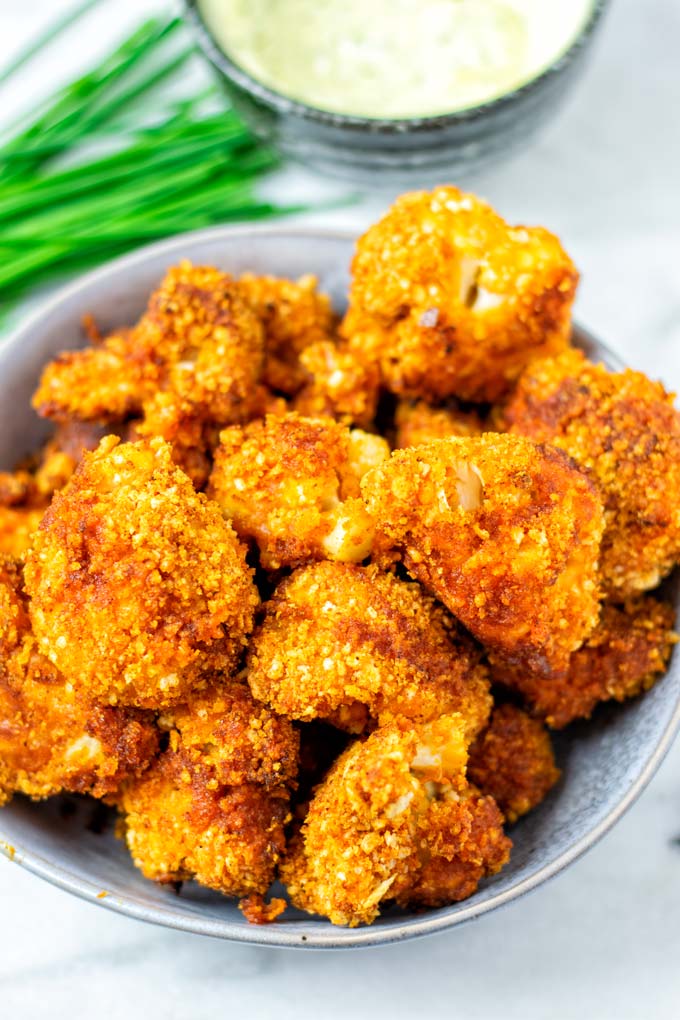 Serving bowl with ready baked Cauliflower Wings with extra dipping sauce in background.