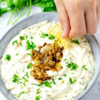 Hand dipping a potato ship into the French Onion Dip.