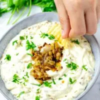 Hand dipping a potato ship into the French Onion Dip.