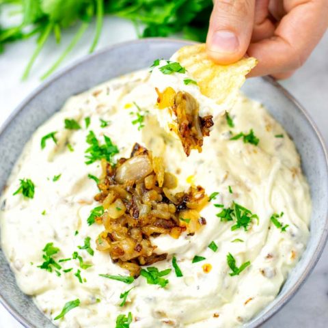 Hand holding a potato chip with French Onion Dressing and extra caramelized onions.