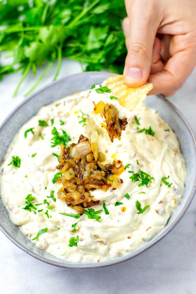 Hand holding a potato chip with French Onion Dressing and extra caramelized onions.