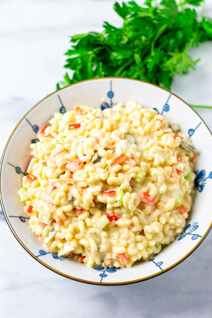 The creamy Macaroni Salad in a white bowl with fresh cilantro in the background.