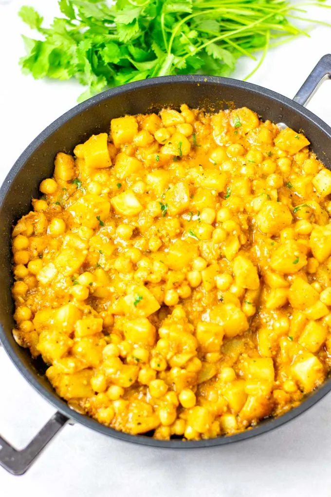 The Potato Curry when done in a large pan, some fresh cilantro in the background.