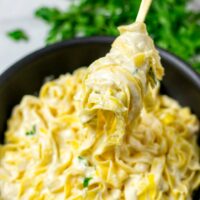 Lifting pasta with Alfredo Sauce from the pan with a fork.