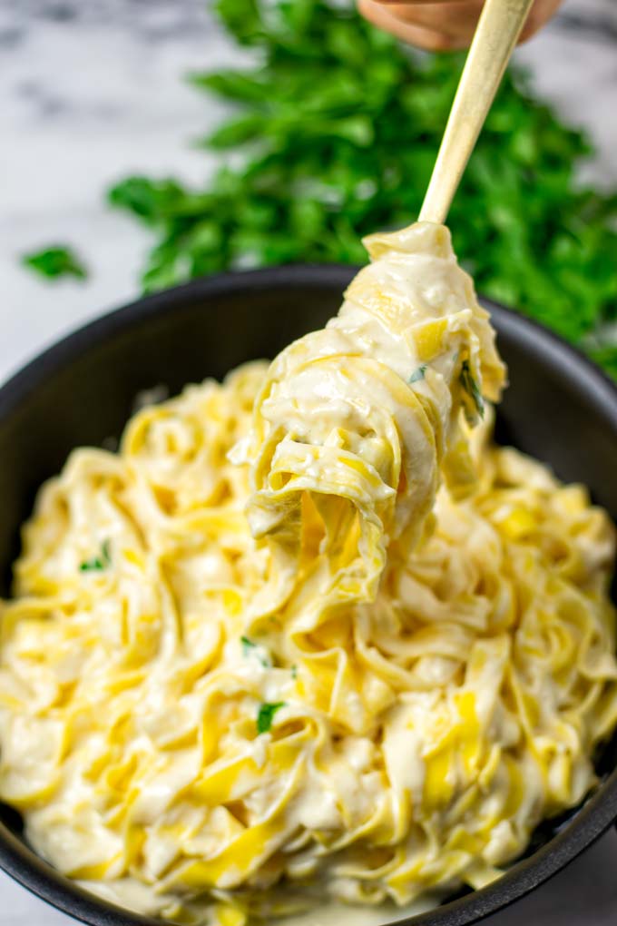 Lifting pasta with Alfredo Sauce from the pan with a fork.