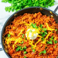 A large pan of the Texas Chili in a frying pan, garnished with vegan sour cream, vegan cheddar and cilantro.