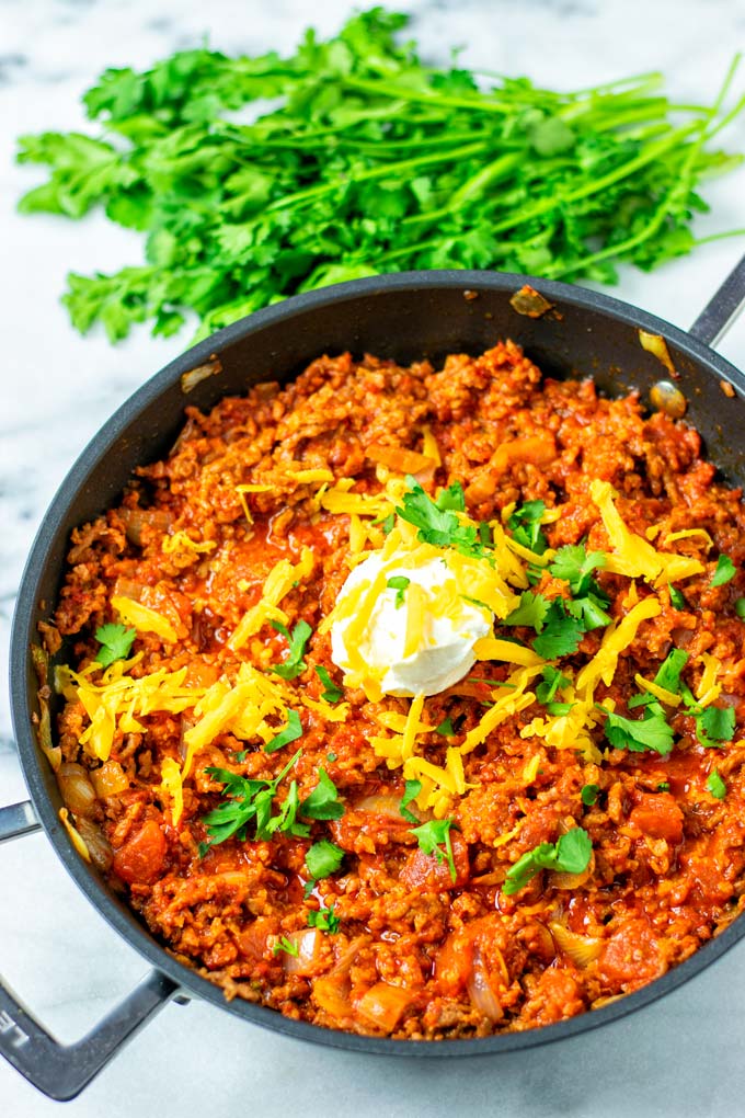 A large pan of the Texas Chili in a frying pan, garnished with vegan sour cream, vegan cheddar and cilantro. 