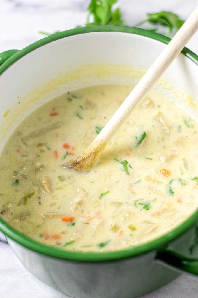 Pot of mixed Avgolemono Soup with a wooden spoon.