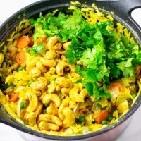 Fresh cilantro is used to garnish the Curried Rice in a large pot.