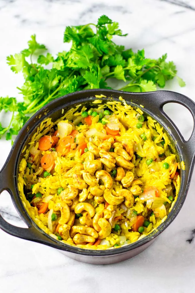 The Curried Rice is finished in a sauce pan, with some fresh cilantro in the background.