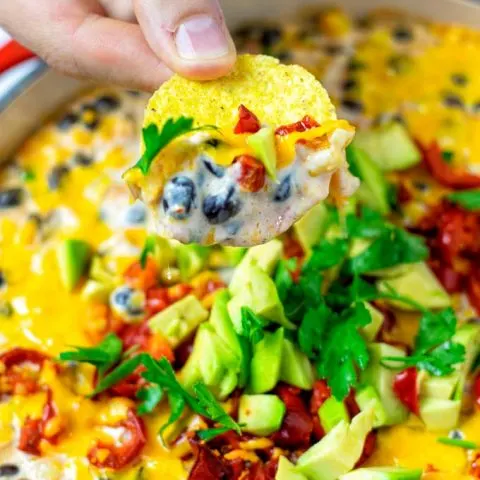 Hand holding a nacho chip with the dip over the casserole dish.