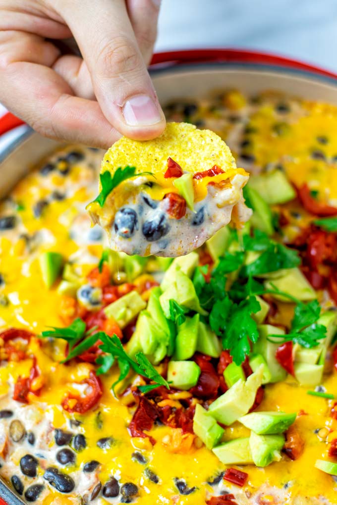 Hand holding a nacho chip with the dip over the casserole dish.