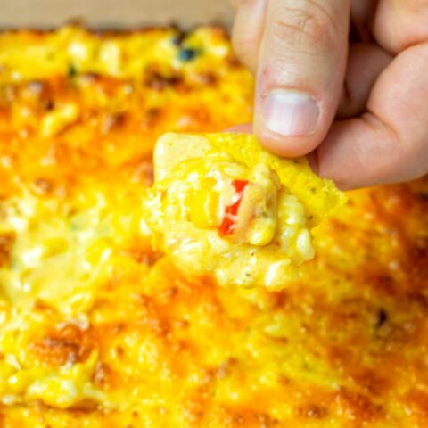 A hand is dipping a tortilla chip into the Corn dip.
