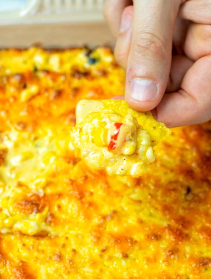 A hand is dipping a tortilla chip into the Corn dip.