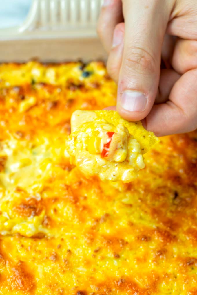 A hand is dipping a tortilla chip into the Corn dip.