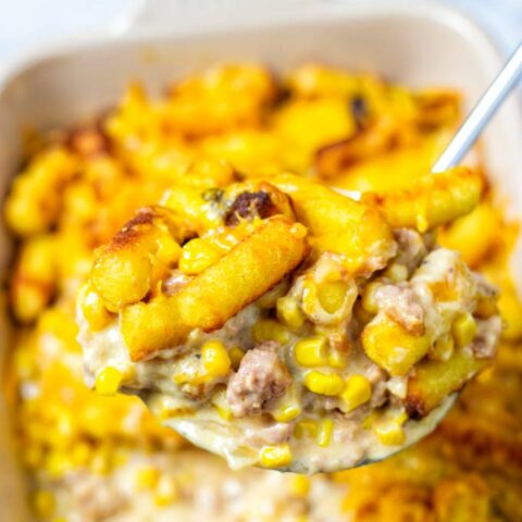 A large portion of the Cowboy Casserole is lifted out of the dish, showing the meaty sauce and tater tots.