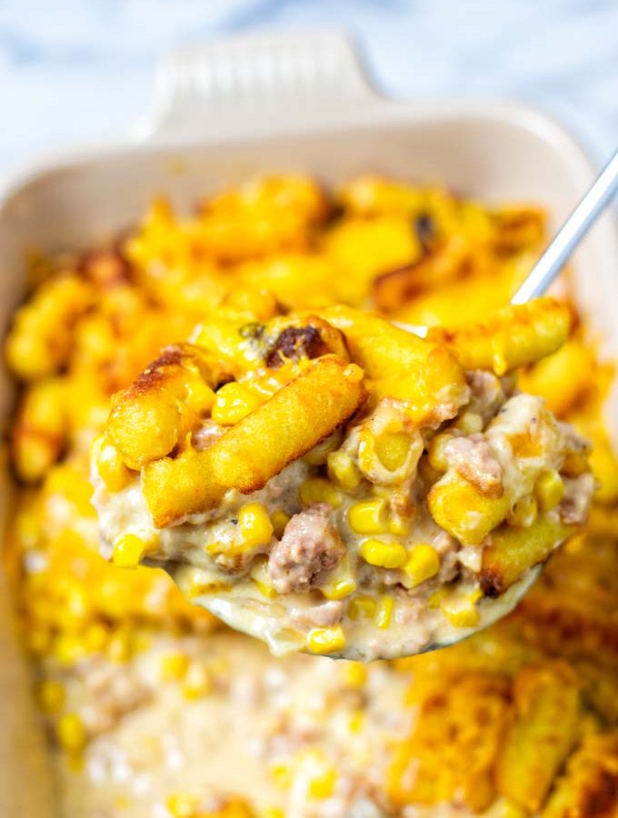 A large portion of the Cowboy Casserole is lifted out of the dish, showing the meaty sauce and tater tots.