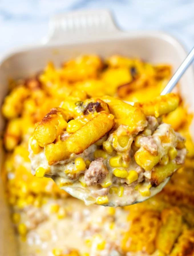 A large portion of the Cowboy Casserole is lifted out of the dish, showing the meaty sauce and tater tots.