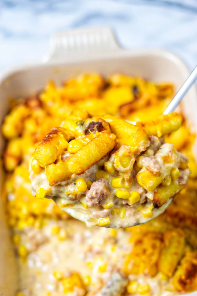 A large portion of the Cowboy Casserole is lifted out of the dish, showing the meaty sauce and tater tots.