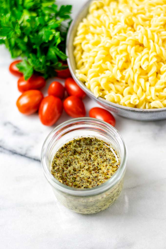 Italian Dressing in a small glass jar in front of a plate of pasta. 