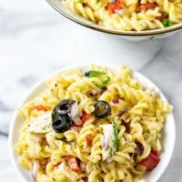 Closeup view of a portion of the Italian Pasta Salad on a small white plate with a serving bowl in the background.