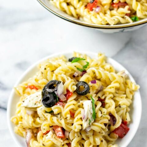 Closeup view of a portion of the Italian Pasta Salad on a small white plate with a serving bowl in the background.