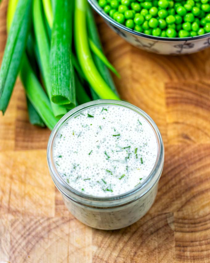 Ranch Dressing in a small glass jar in front of green peas.