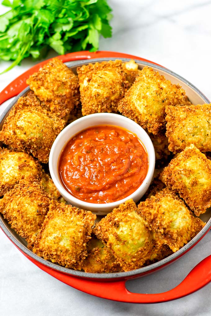 A whole dish full of Toasted Ravioli with a small bowl of marinara sauce.