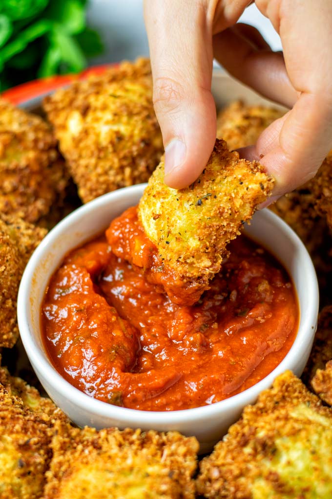 Closeup of a Toasted Ravioli dipped into marinara sauce.