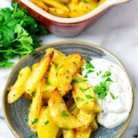 A portion of the Greek Lemon Potatoes on a small plate served with dipping sauce.