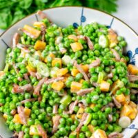 Pea Salad in a large serving bowl with some fresh herbs in the background.