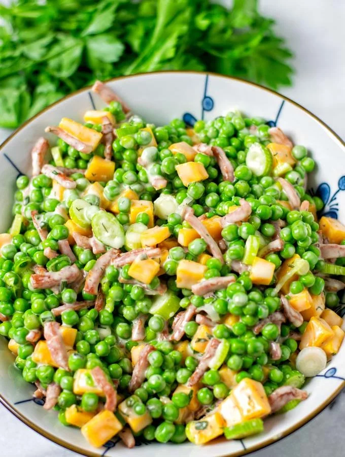 Pea Salad in a large serving bowl with some fresh herbs in the background.