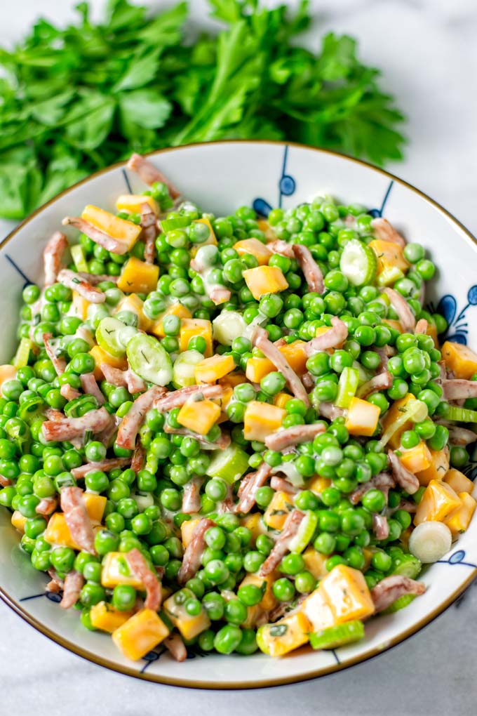 Pea Salad in a large serving bowl with some fresh herbs in the background.