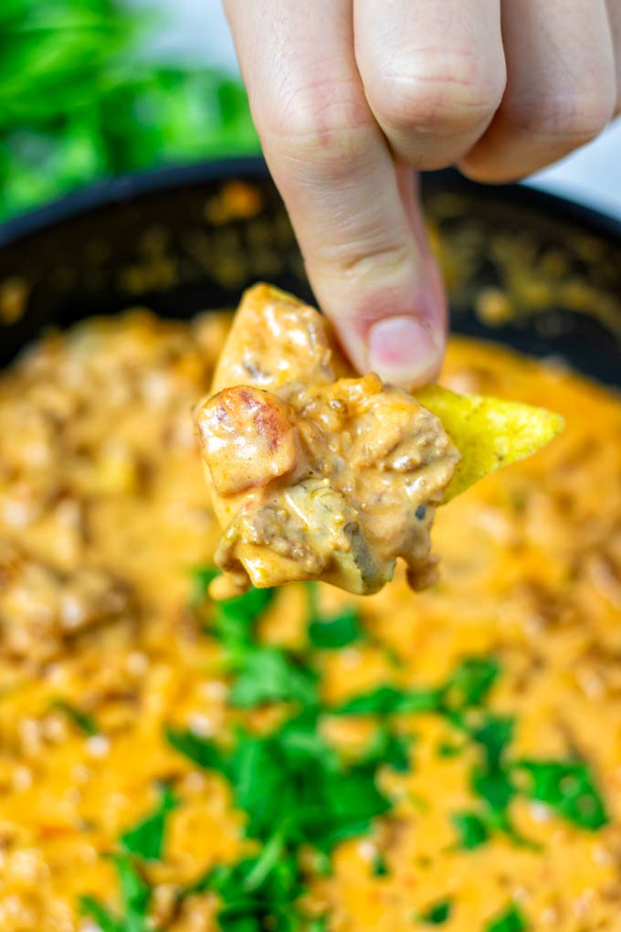 Closeup on the Rotel Dip on the nacho chip being held between fingers.