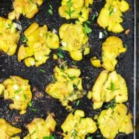 Smashed Potatoes on a bkaing sheet after baking, garnished with some fresh herbs.