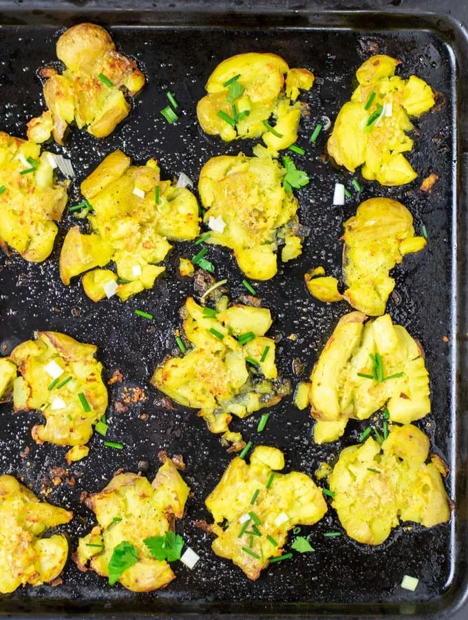 Smashed Potatoes on a bkaing sheet after baking, garnished with some fresh herbs.