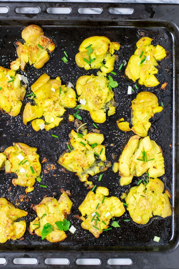 Smashed Potatoes on a baking sheet after baking, garnished with some fresh herbs.