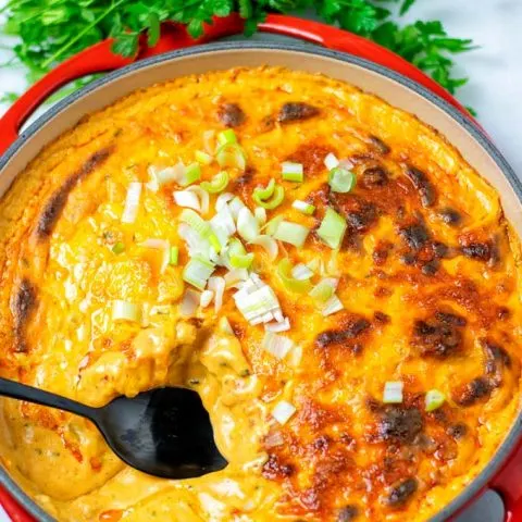 Casserole dish with the vegan Buffalo Dip with a black spoon sticking in it.